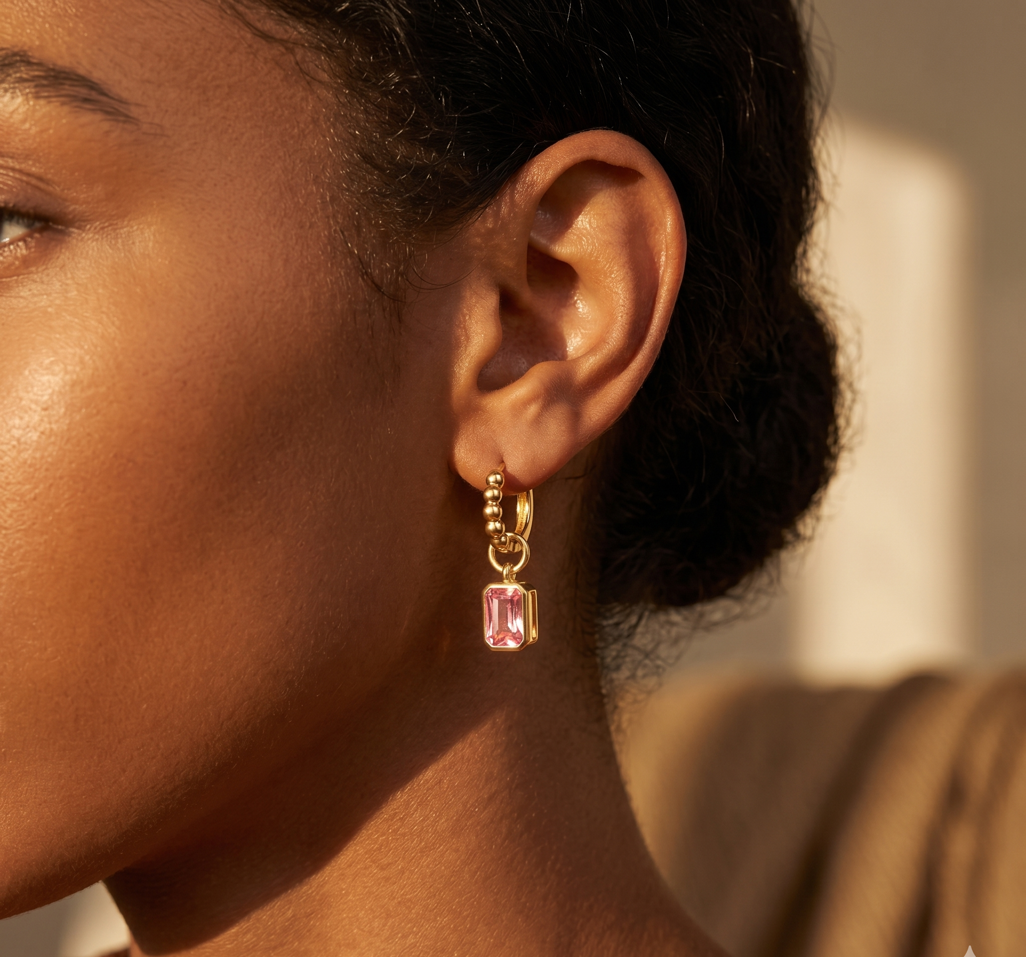 Close-up of a person wearing pink gemstone earrings with gold hooks.