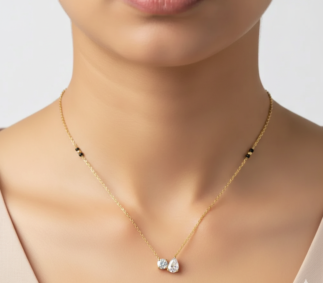 Gold necklace with two teardrop-shaped gemstones worn by a person on a neutral background
