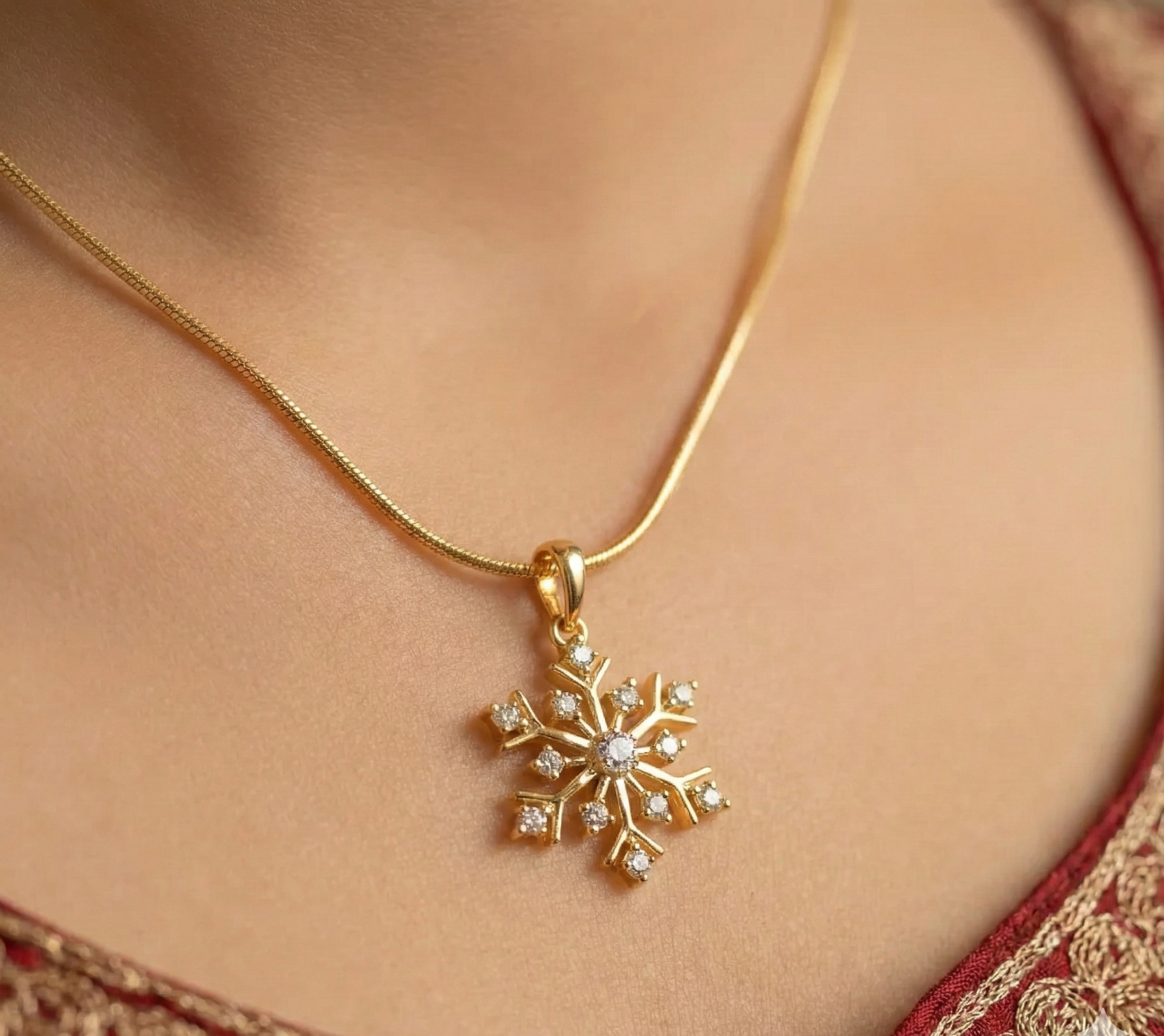 Gold necklace with a snowflake pendant on a person wearing a red and gold embroidered garment.