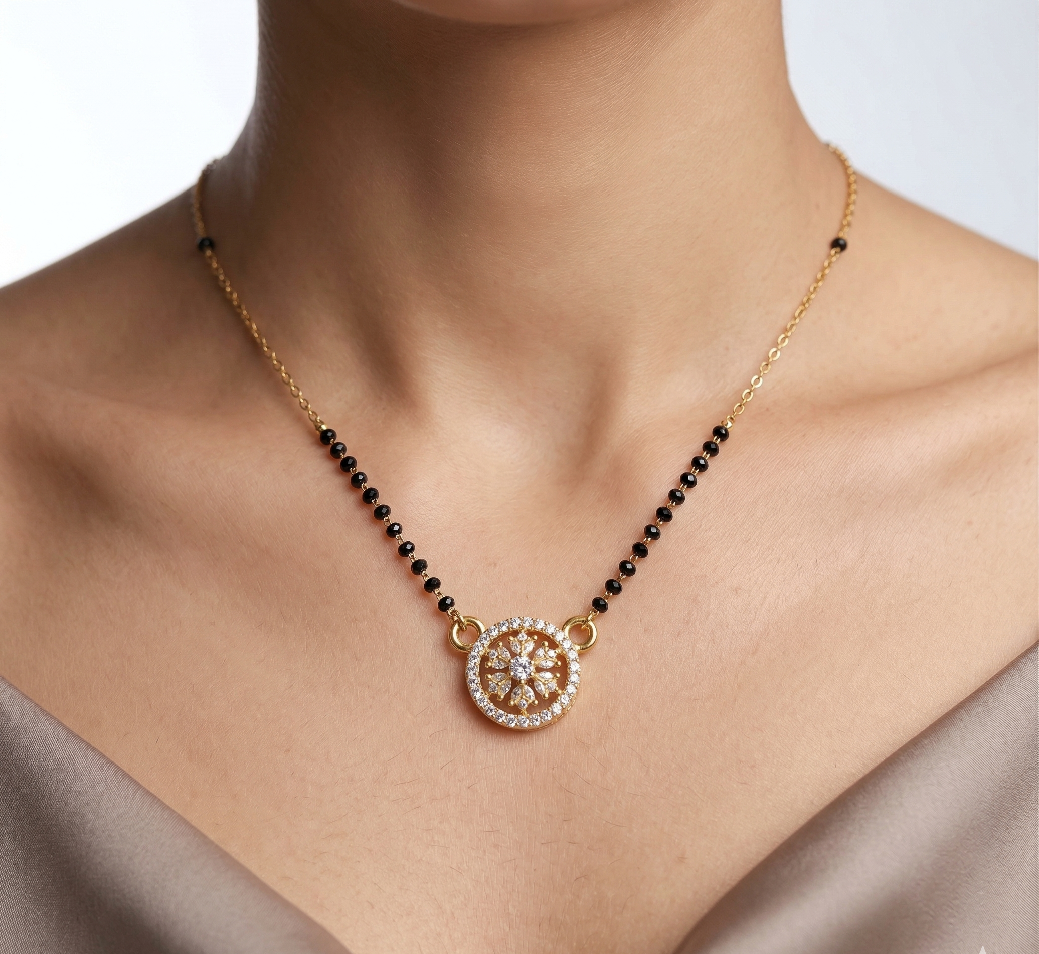 Necklace with black beads and a gold pendant on a person wearing a beige top.