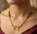 Gold necklace with black beads on a person wearing a maroon saree.