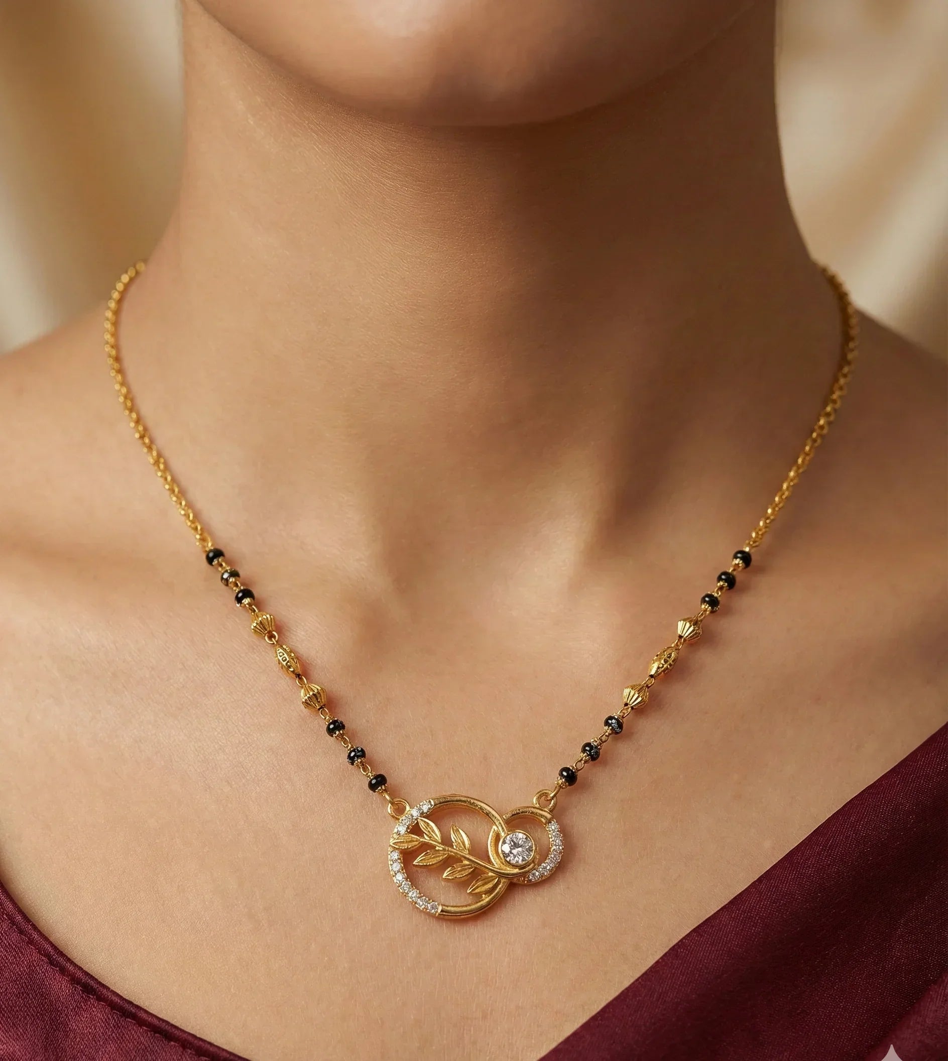 Gold necklace with a circular pendant on a person wearing a maroon top.