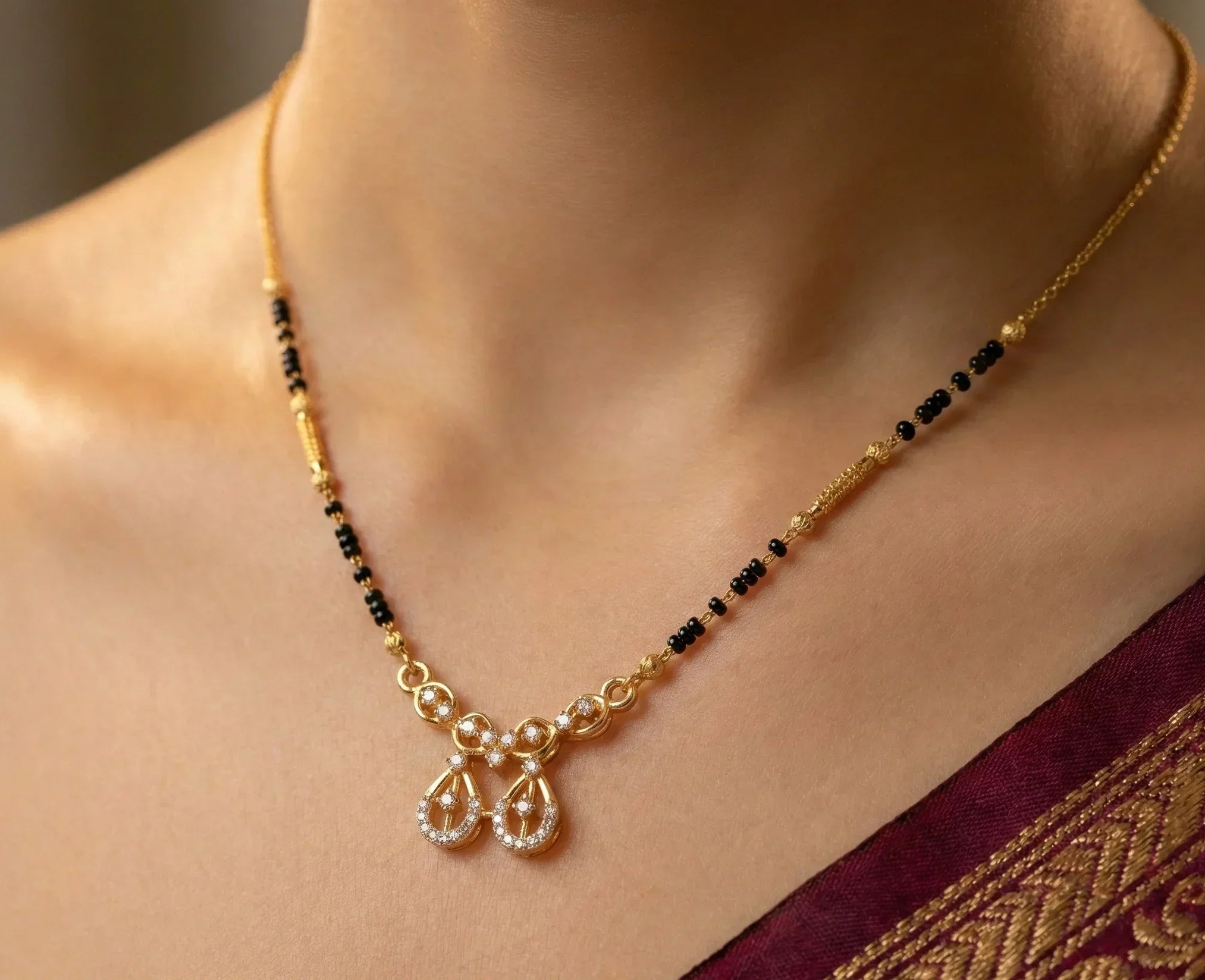 Gold necklace with black beads and a pendant on a person wearing a maroon saree.