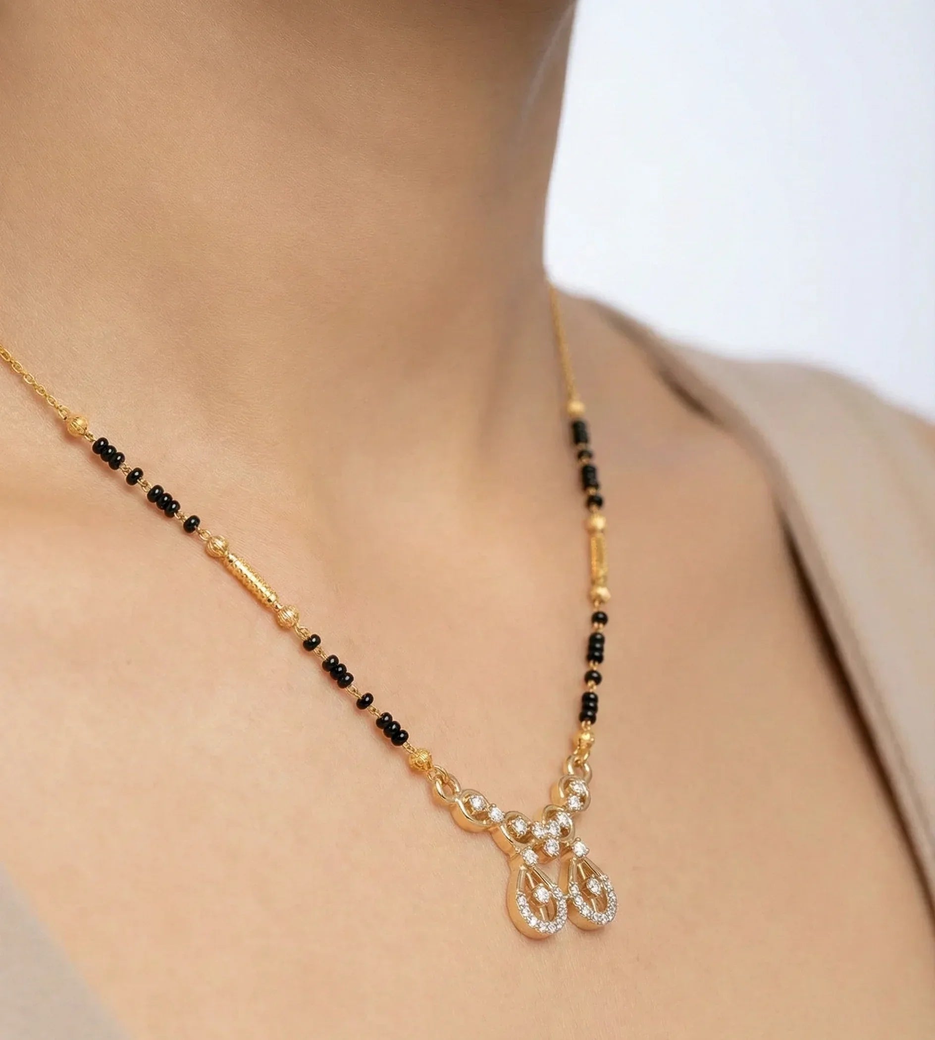 Necklace with black and gold beads on a person wearing a beige top.