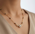 Gold necklace with a floral pendant on a person wearing a beige top.