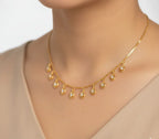 Gold necklace with teardrop-shaped pendants on a mannequin with a beige top.
