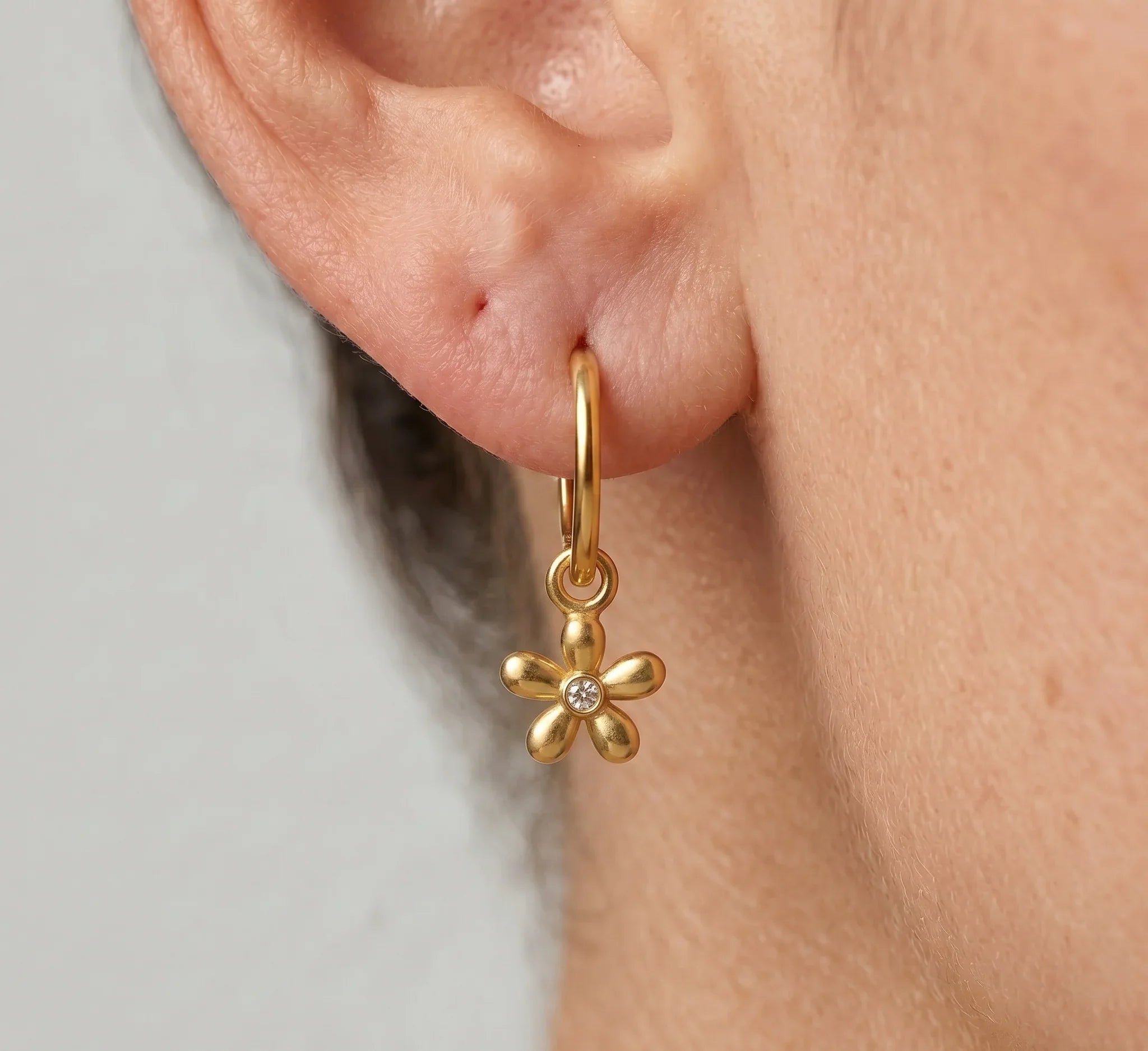 Gold flower-shaped earring worn by a person on a neutral background