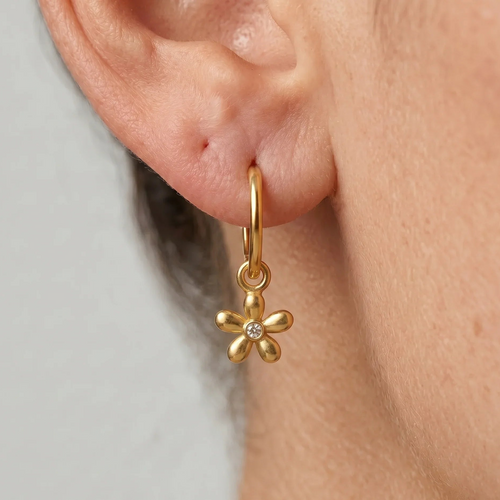 Gold flower-shaped earring worn by a person on a neutral background