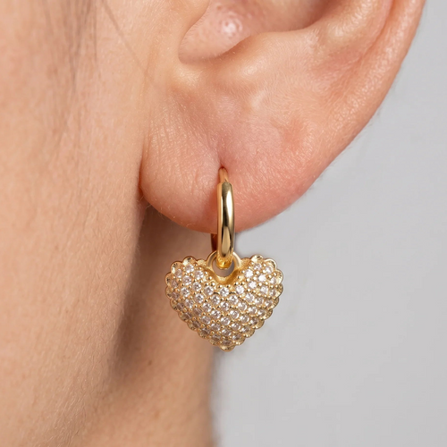 Gold heart-shaped earring worn on an ear with a neutral background