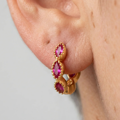 Gold hoop earrings with pink gemstones worn on an ear against a neutral background