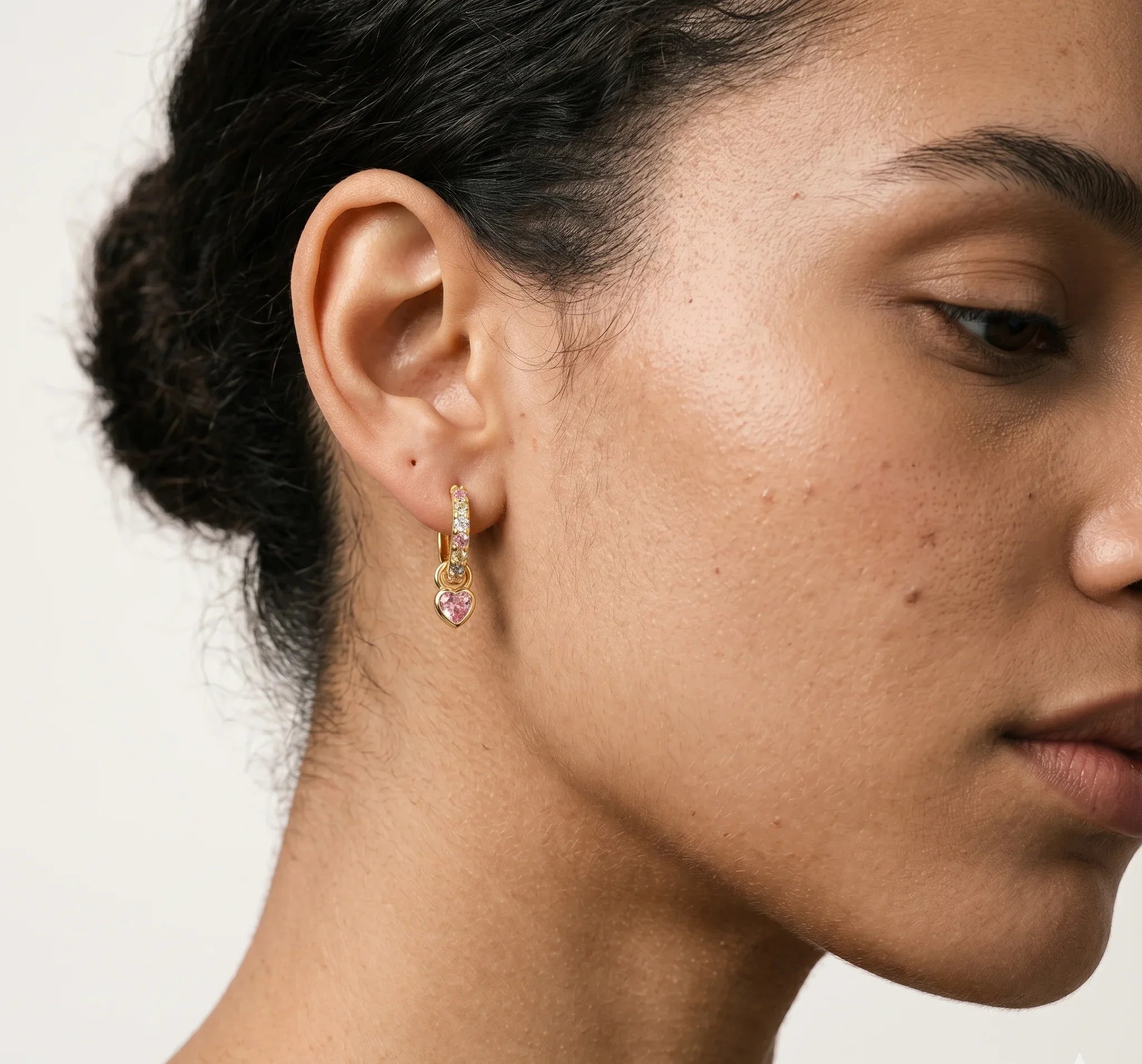 Close-up of a woman wearing a gold earring with pink gemstones on a neutral background