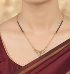 Gold necklace with black beads on a person wearing a maroon saree.