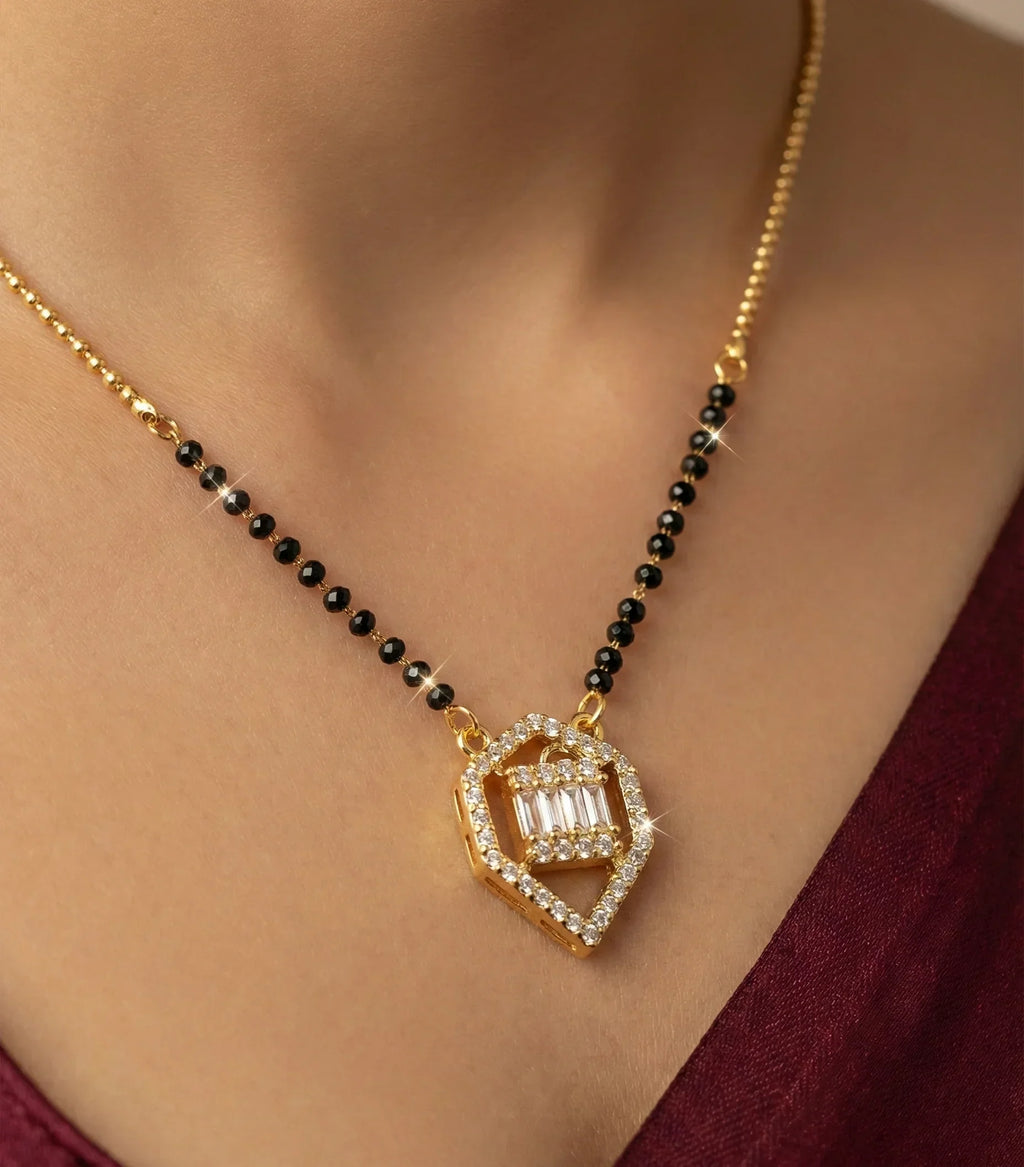 Gold necklace with black beads and a diamond pendant on a person wearing a burgundy top.