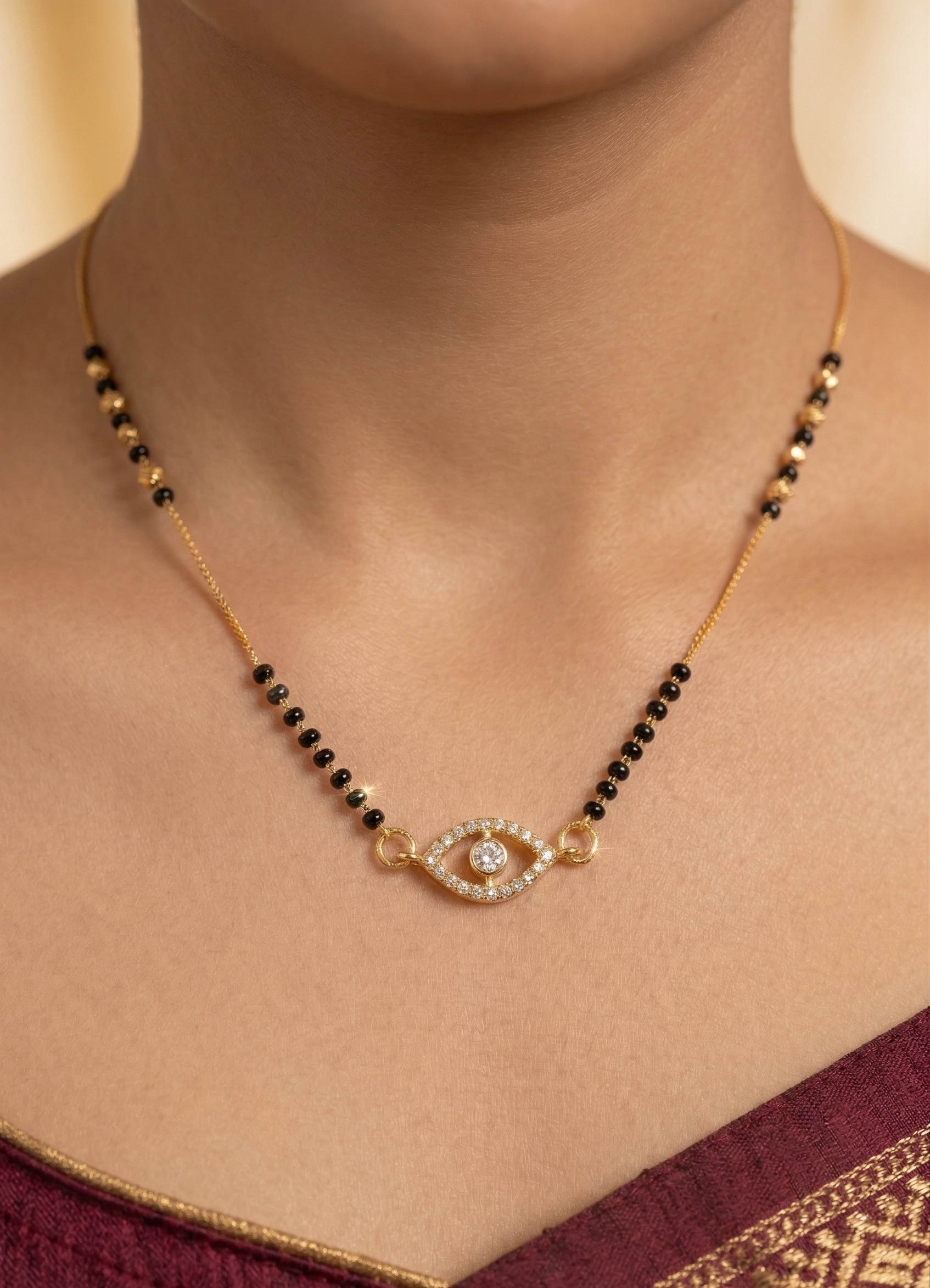 Necklace with black beads and gold evil eye pendant on a person wearing a maroon saree.