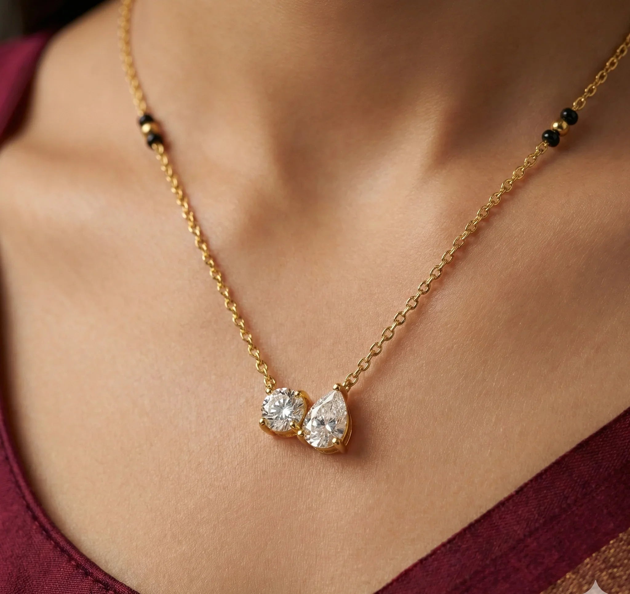 Gold necklace with two teardrop-shaped diamonds on a person wearing a burgundy top.