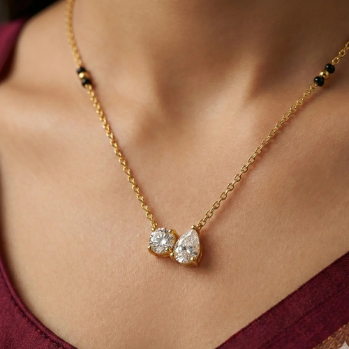 Gold necklace with two teardrop-shaped diamonds on a person wearing a burgundy top.
