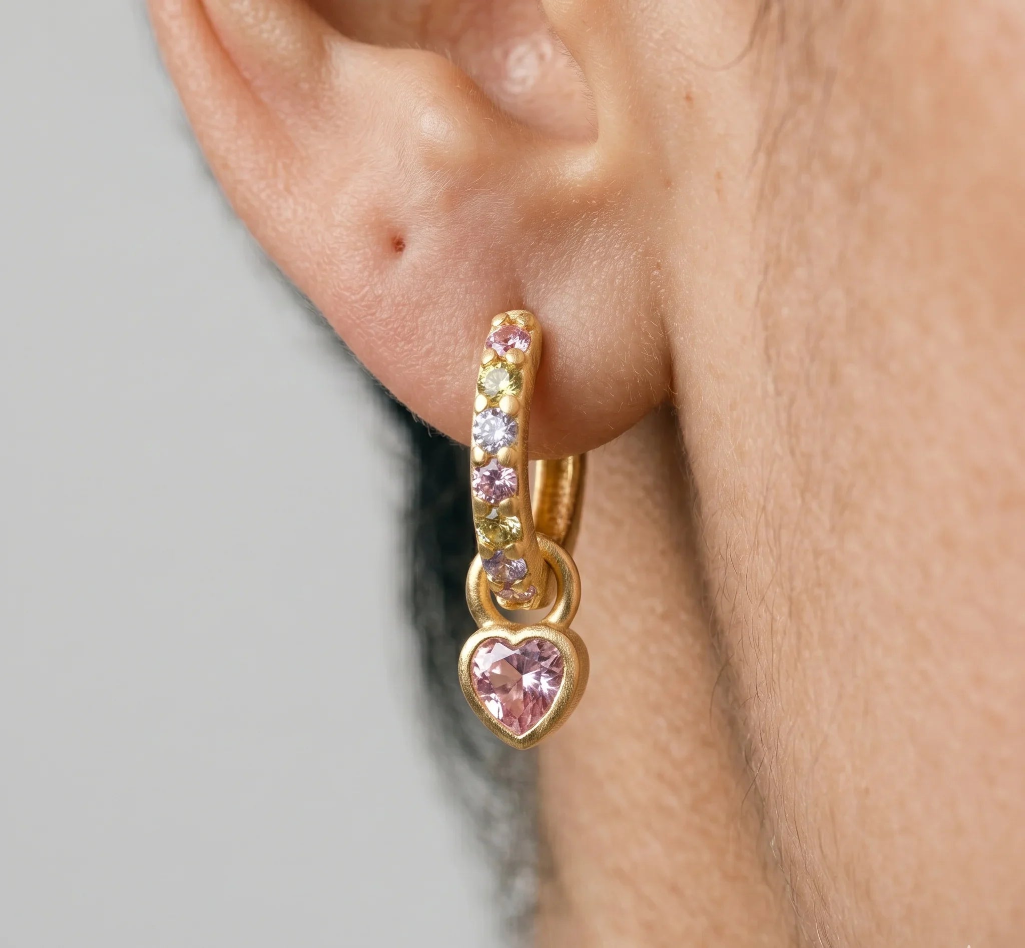 Gold hoop earring with heart-shaped gemstone on a neutral background