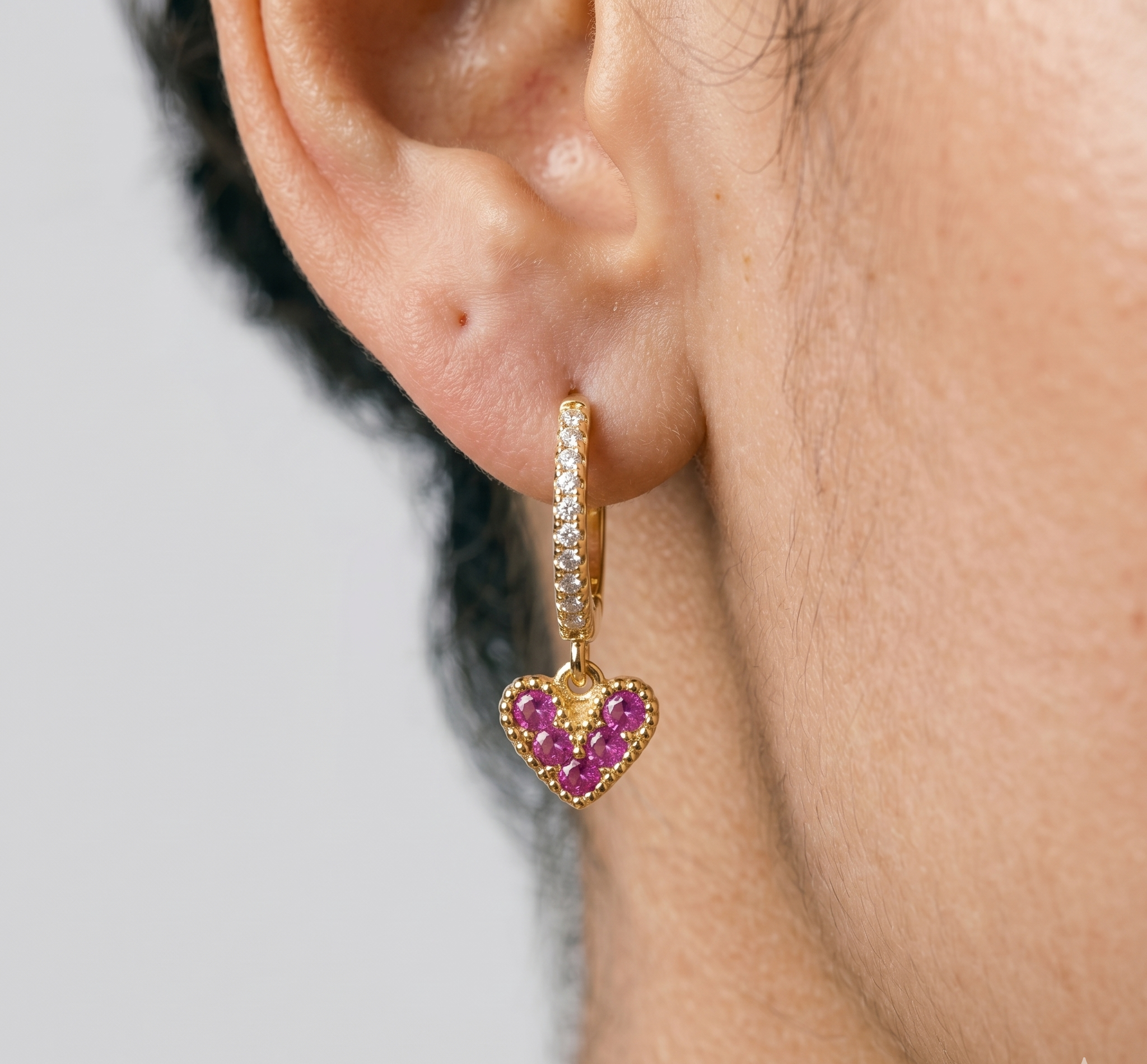 Gold heart-shaped earring with pink gemstones worn by a person.