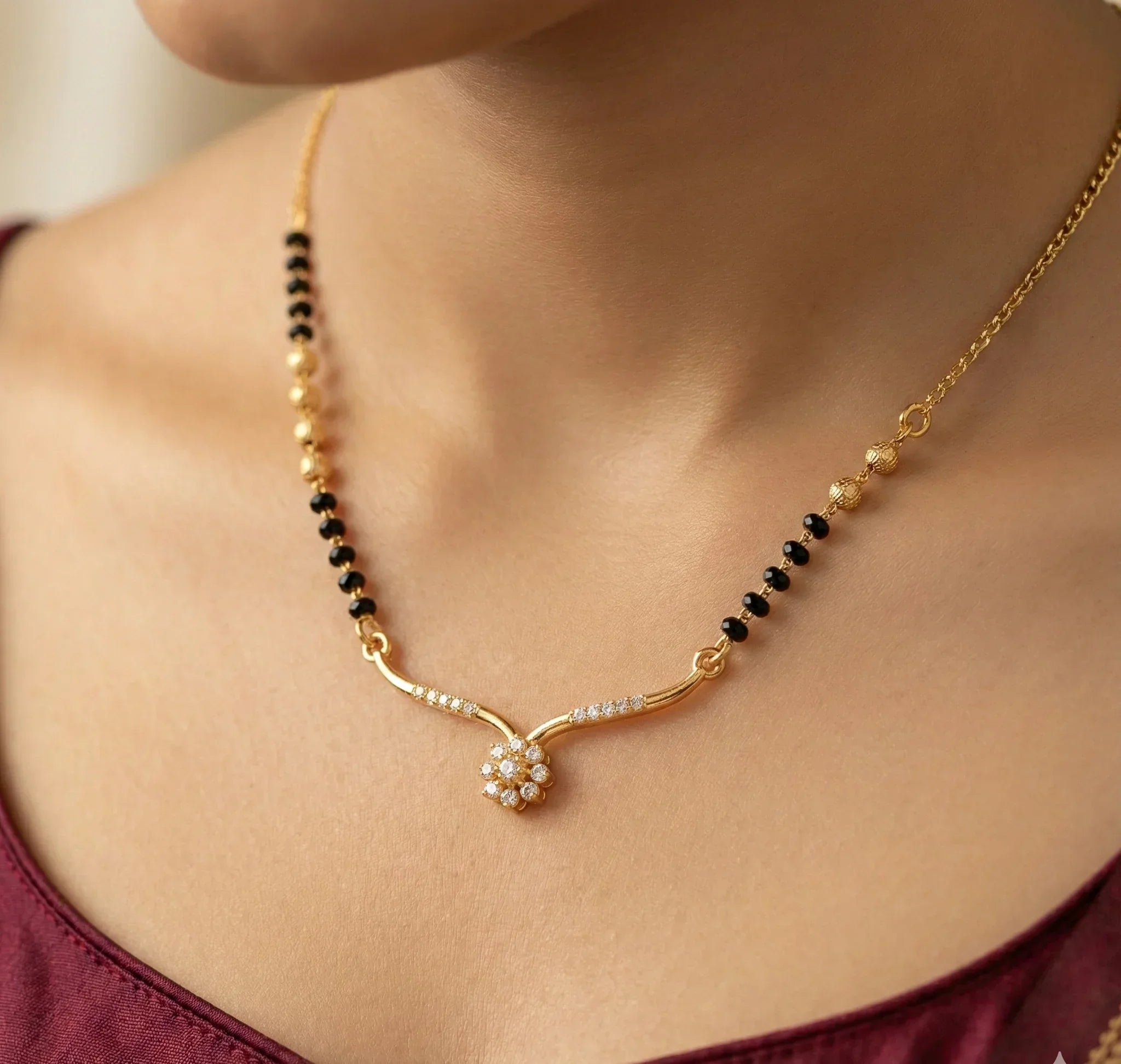 Gold necklace with black beads on a person wearing a burgundy top.