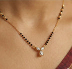 Gold necklace with black beads and a teardrop pendant on a person's neck.