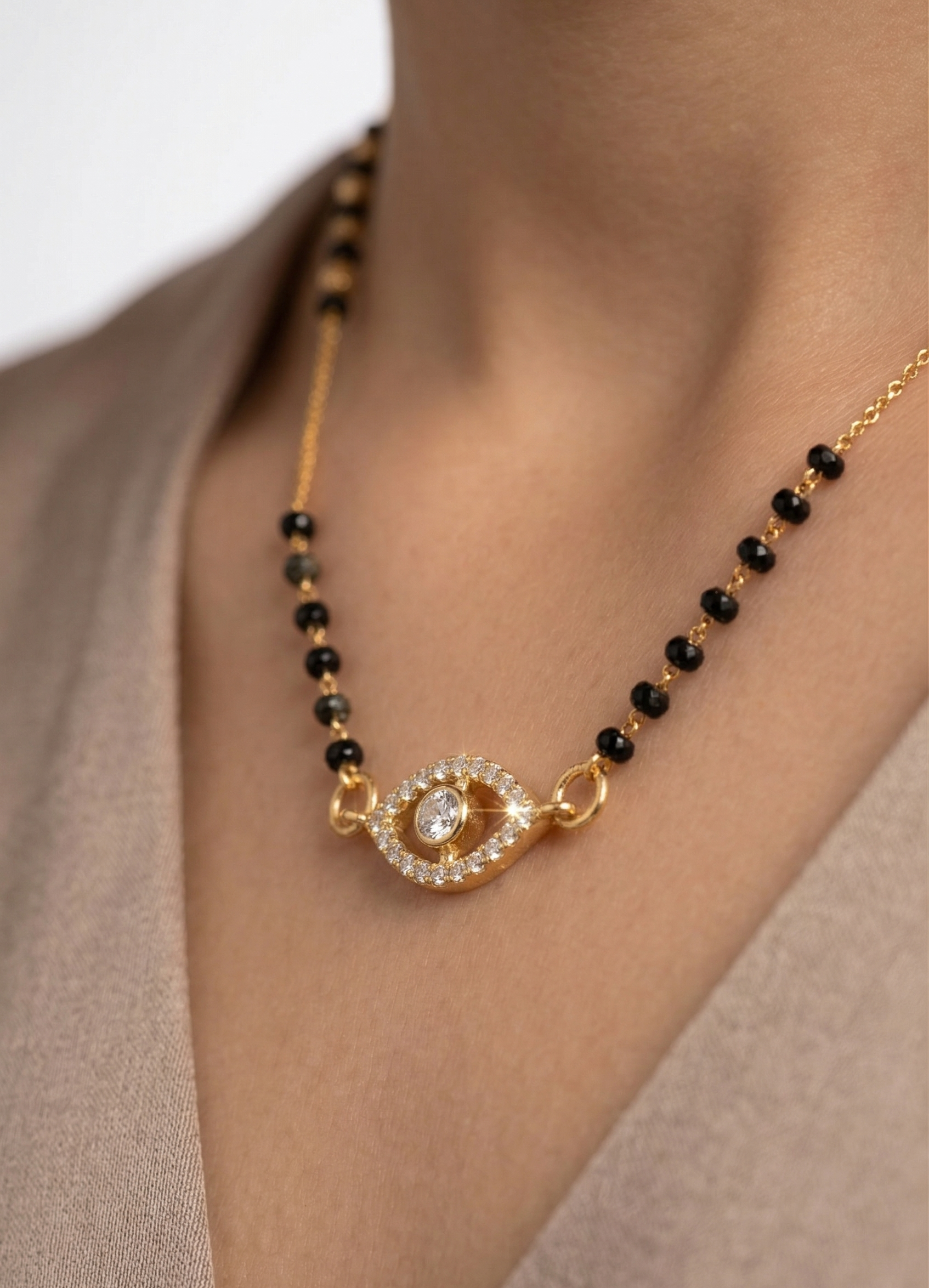 Gold necklace with black beads and a diamond pendant on a neutral background