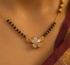 Gold necklace with black beads and a floral pendant on a person wearing a saree.