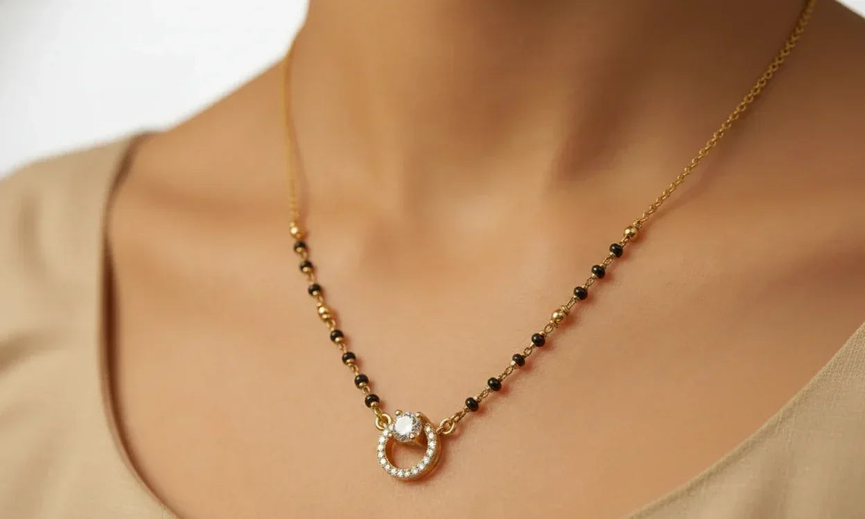 Gold and black beaded necklace with a circular pendant on a person wearing a beige top.