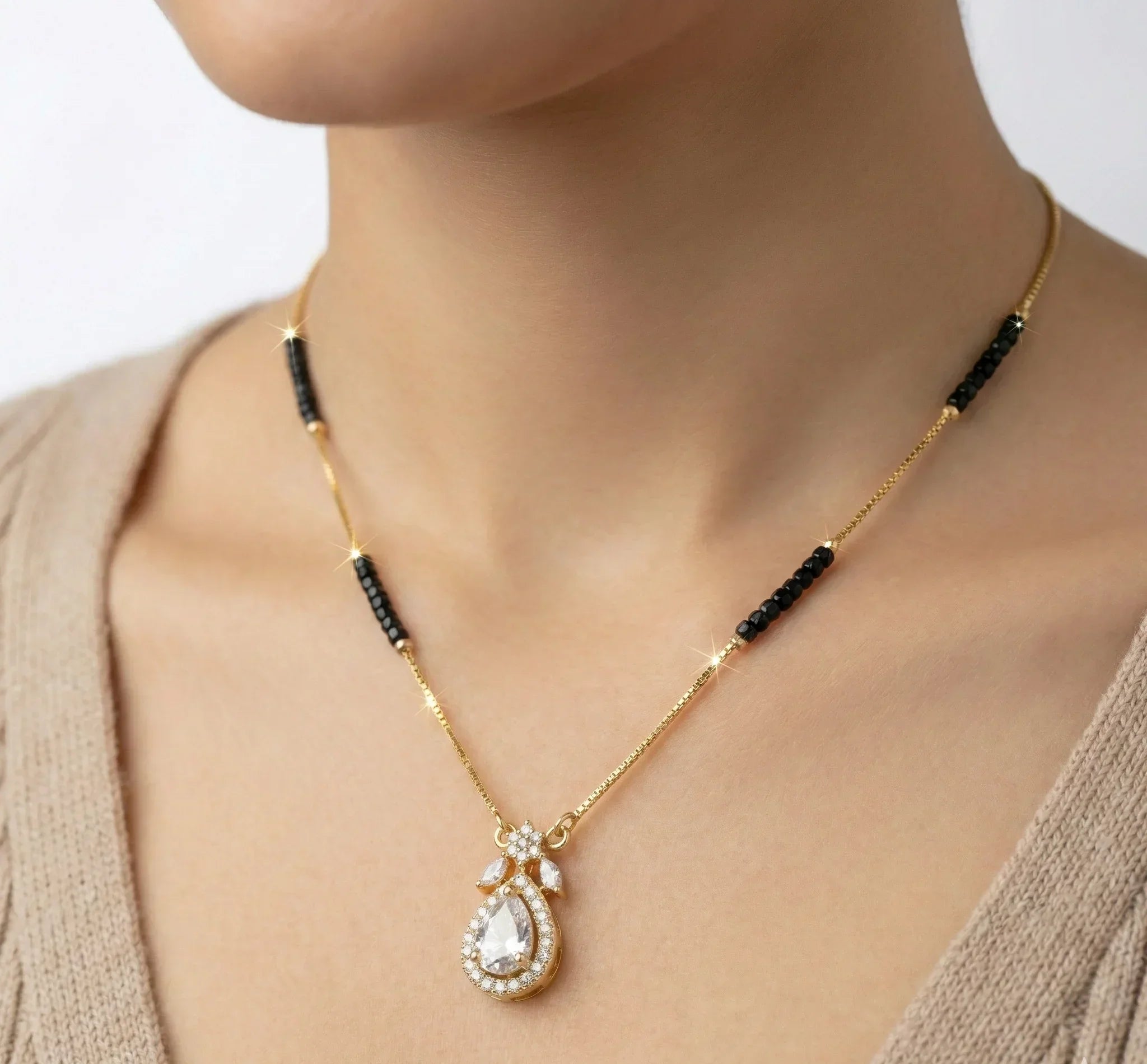 Gold necklace with black beads and a teardrop pendant on a person wearing a beige cardigan.