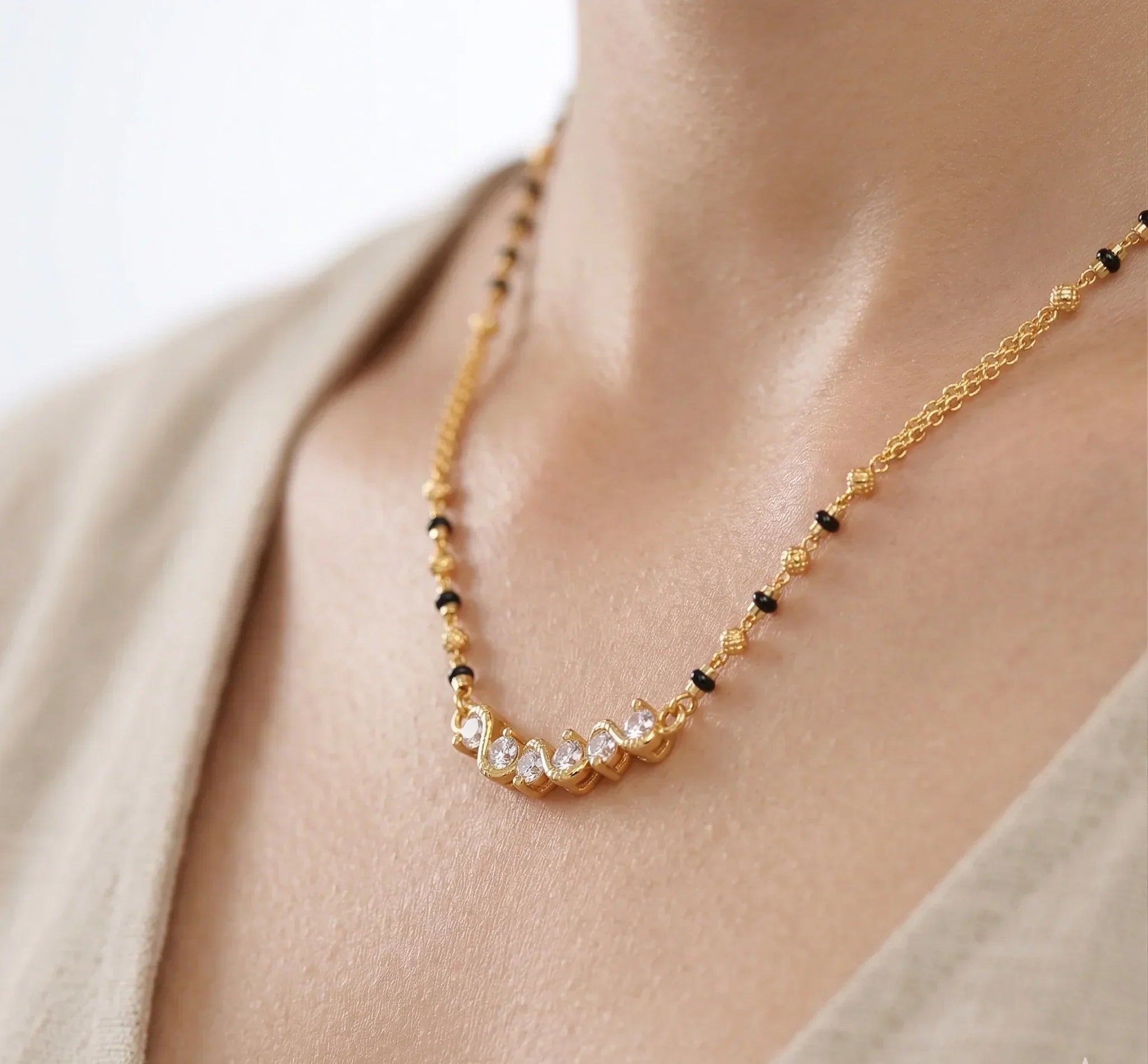 Gold necklace with black beads on a person wearing a beige top.