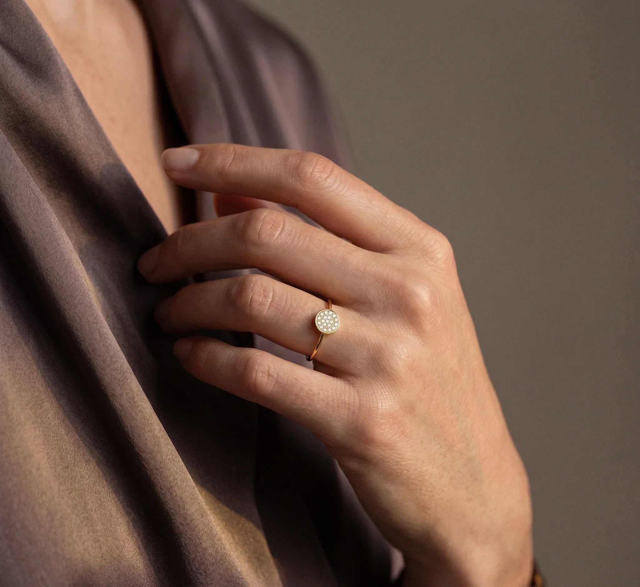 Hand wearing a gold ring with a diamond on a brown fabric background