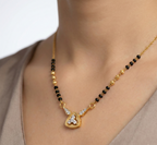 Gold necklace with black beads and a heart-shaped pendant on a person wearing a beige top.
