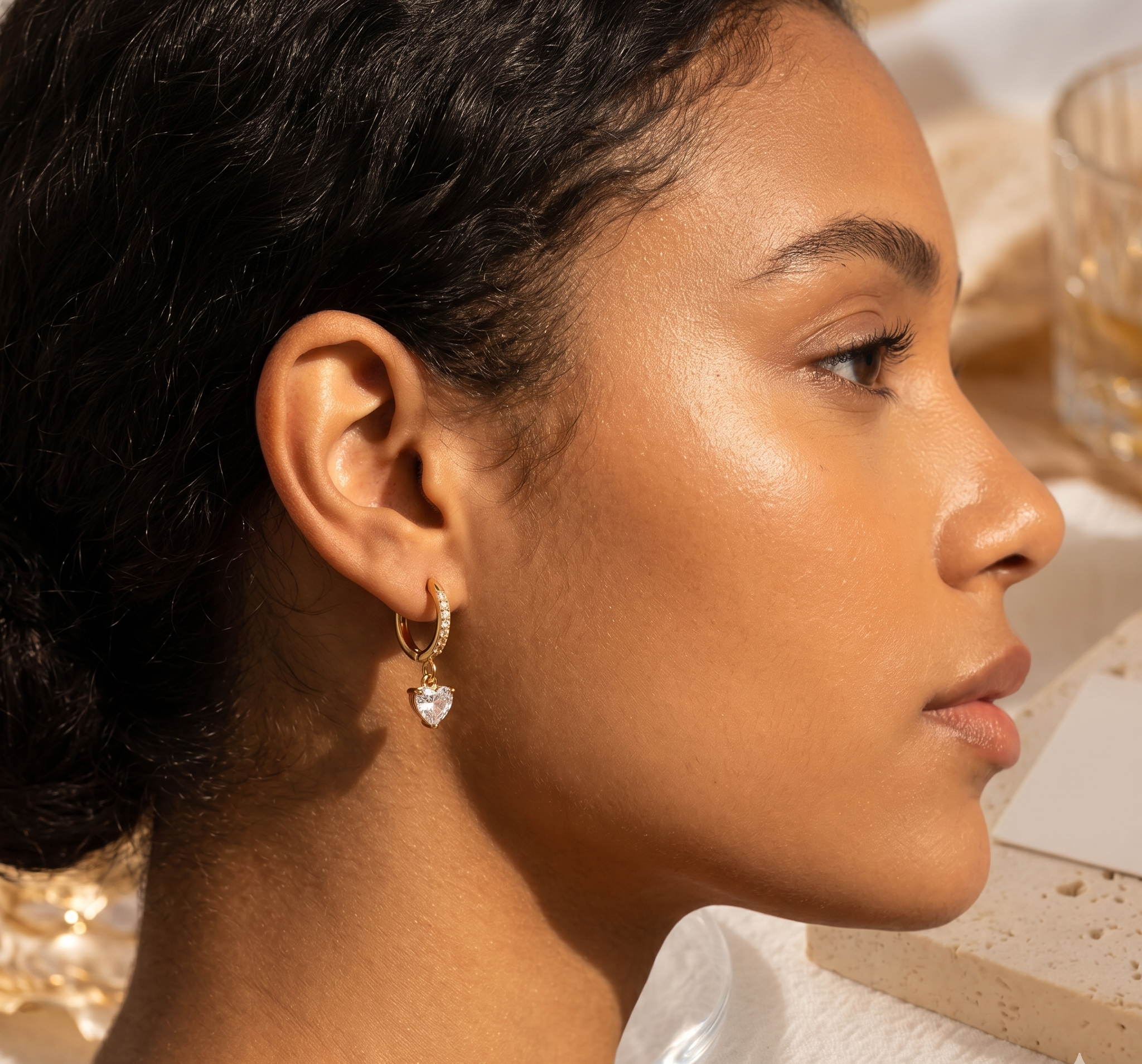 Close-up of a woman wearing gold hoop earrings with a heart-shaped gemstone.