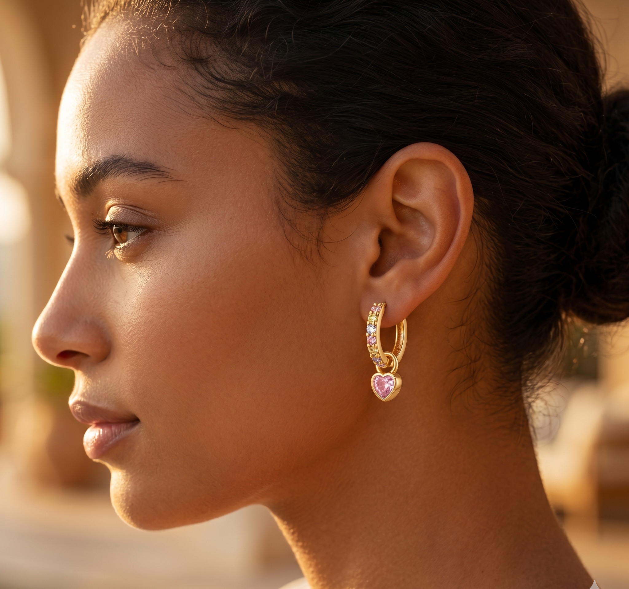 Close-up of a woman wearing a gold hoop earring with a heart-shaped pink gemstone.