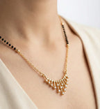 Gold necklace with black beads on a person wearing a white top