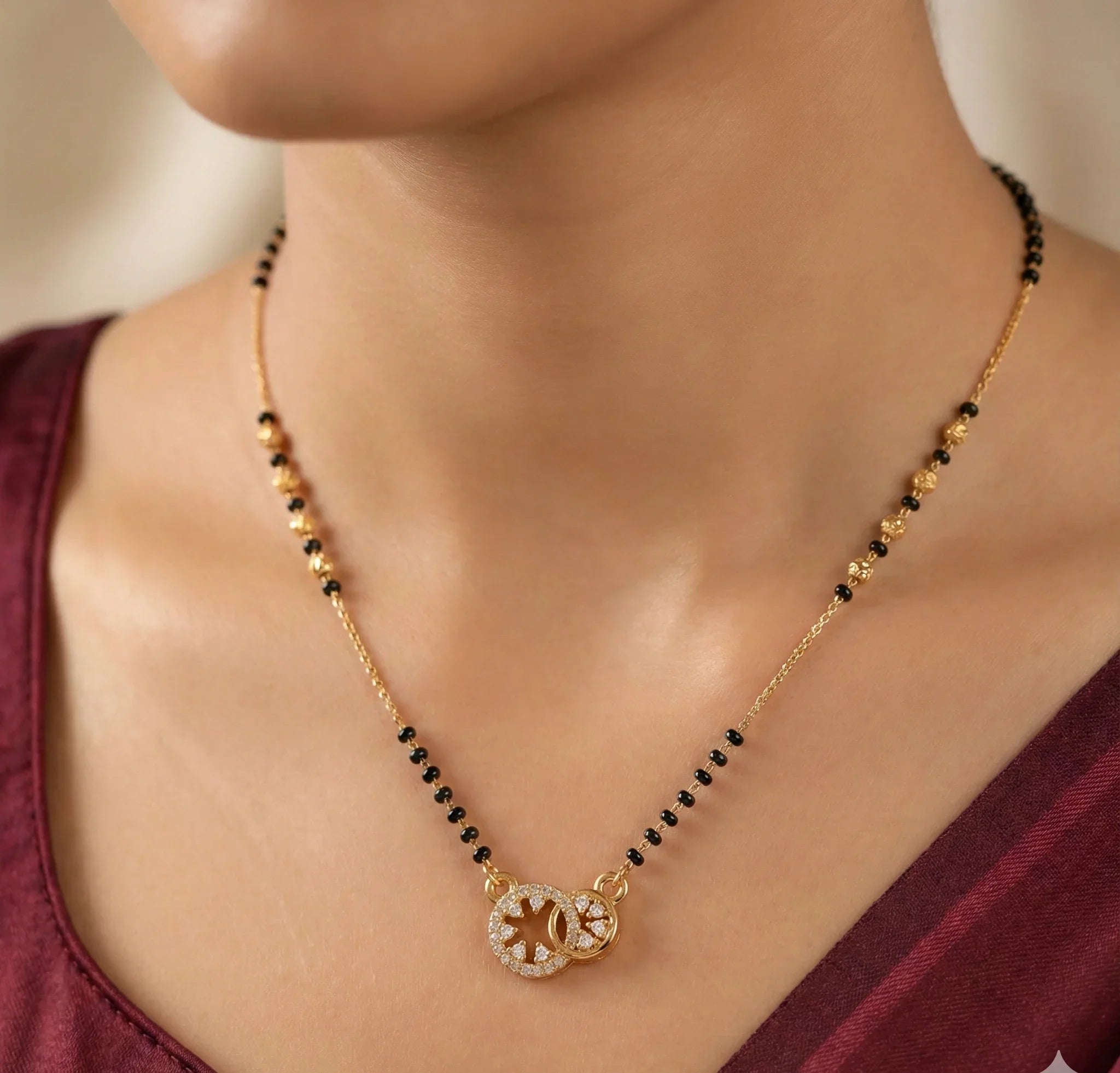 Gold and black beaded necklace worn by a person in a burgundy top.