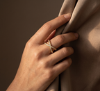 Hand wearing a gold ring with a diamond on a brown background
