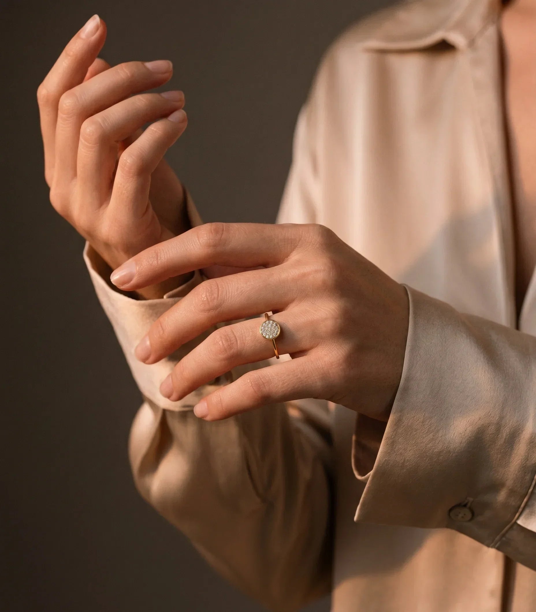 Close-up of a person wearing a beige shirt with a ring on their finger against a dark background