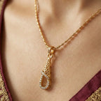 Gold necklace with a teardrop pendant on a person wearing a maroon and gold outfit.