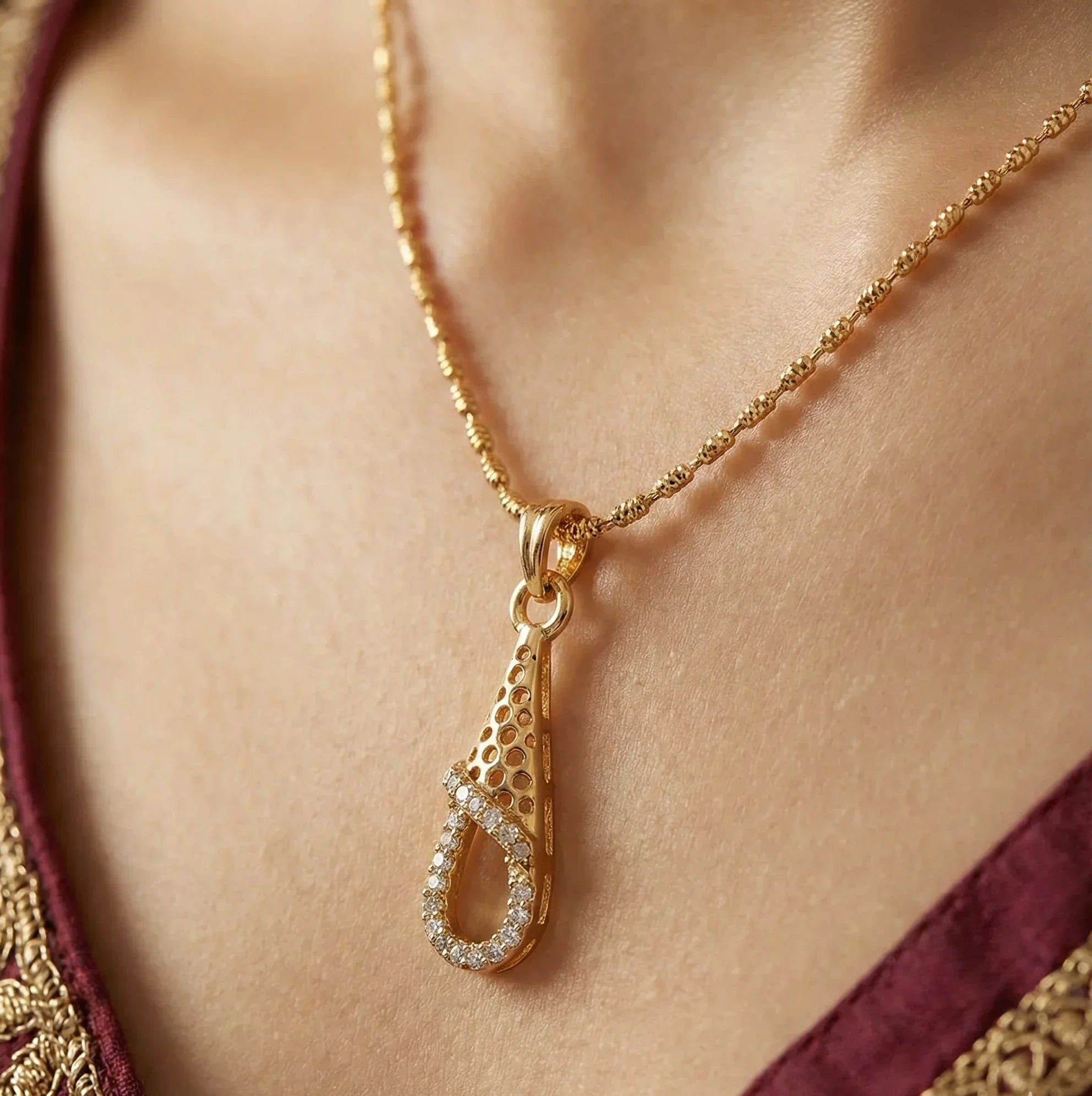 Gold necklace with a teardrop pendant on a person wearing a maroon and gold outfit.
