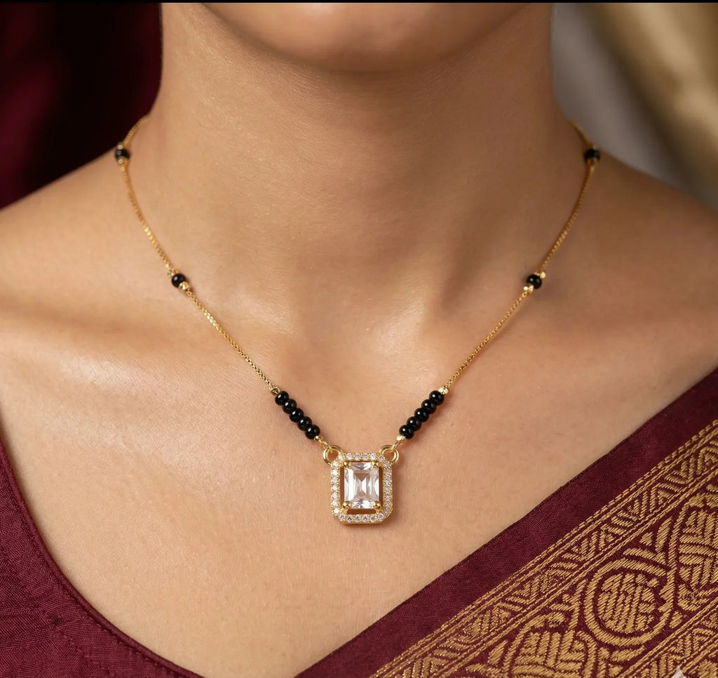 Gold necklace with a pendant worn by a person in a maroon saree.