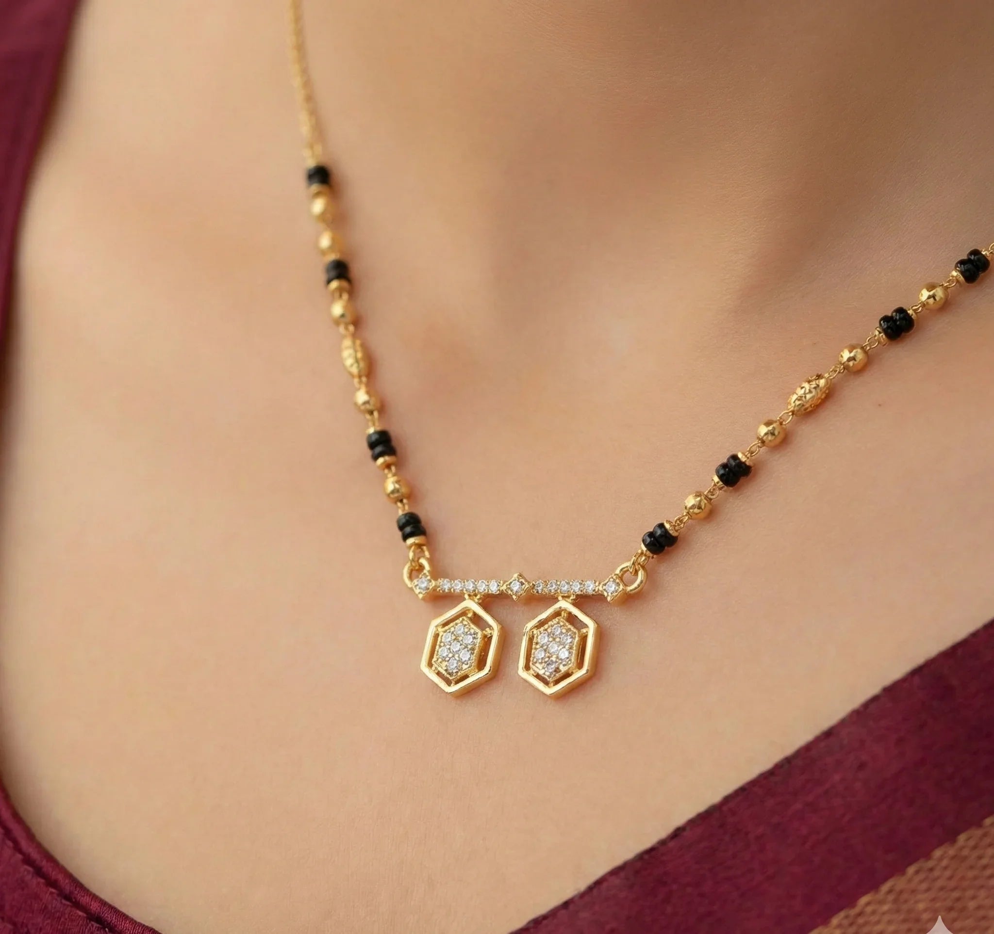 Gold necklace with black beads and diamond-like pendants on a person wearing a maroon top.