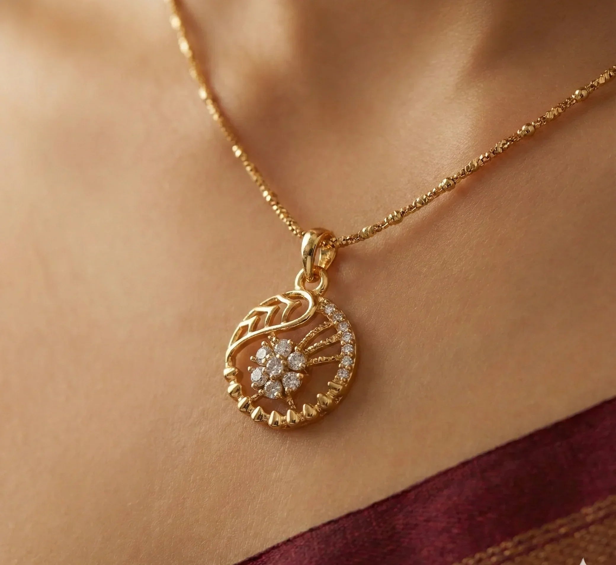 Gold necklace with a diamond pendant on a person wearing a maroon saree.