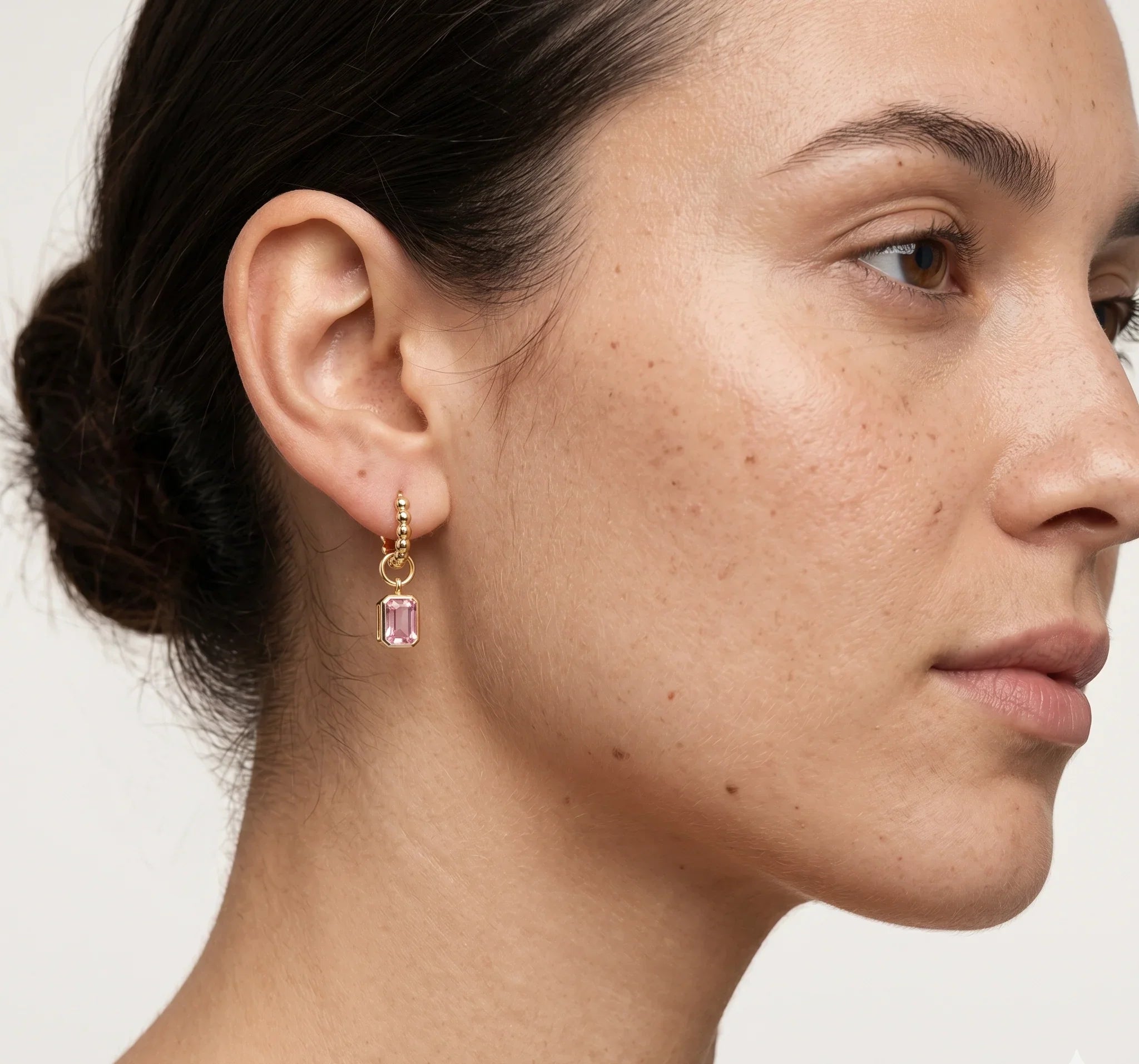 Close-up of a woman wearing a gold earring with a pink gemstone on a white background