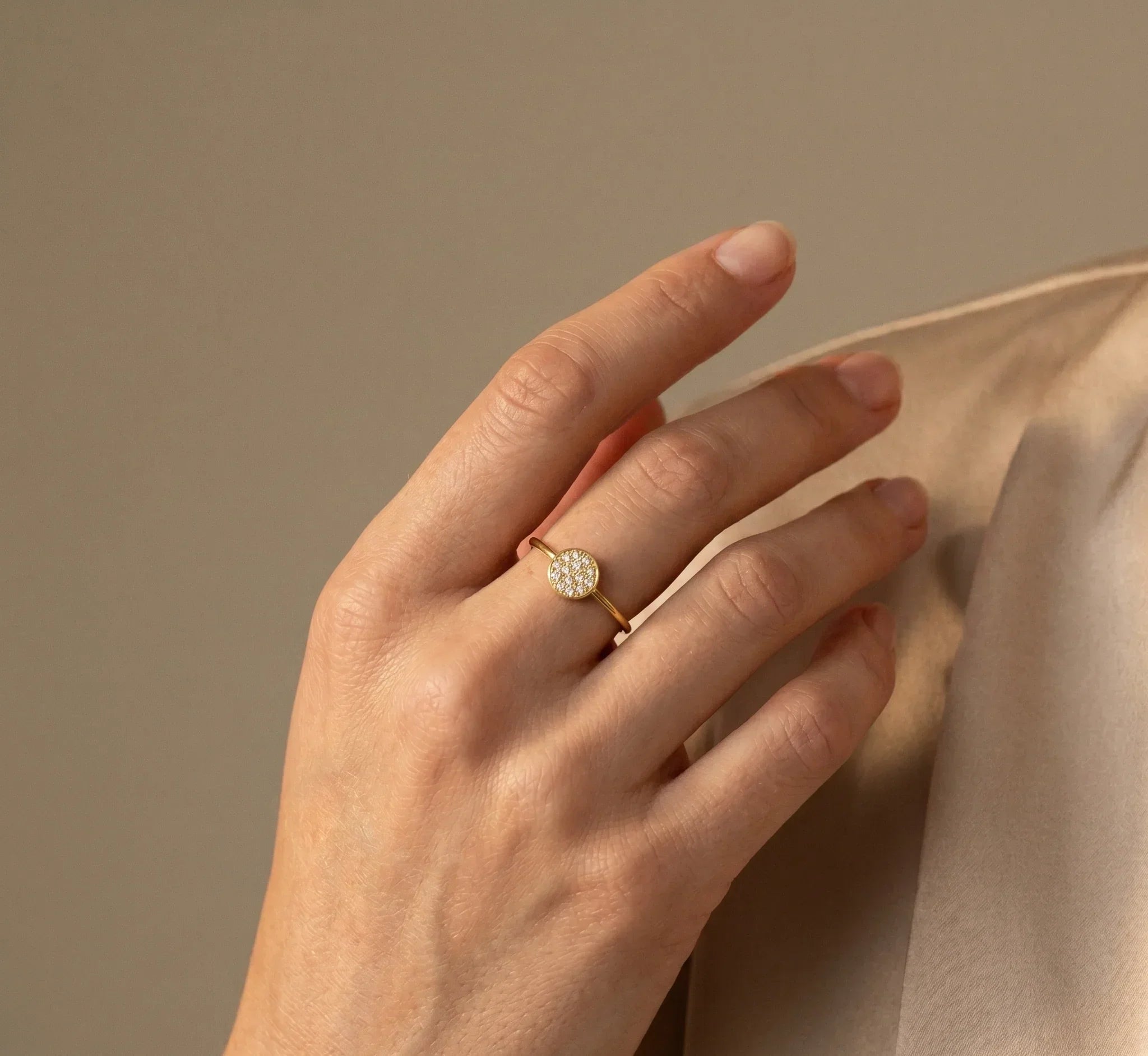 Hand wearing a rose gold ring with a diamond on a beige background