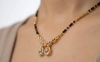 Gold necklace with black beads and pendants on a person wearing a beige top.