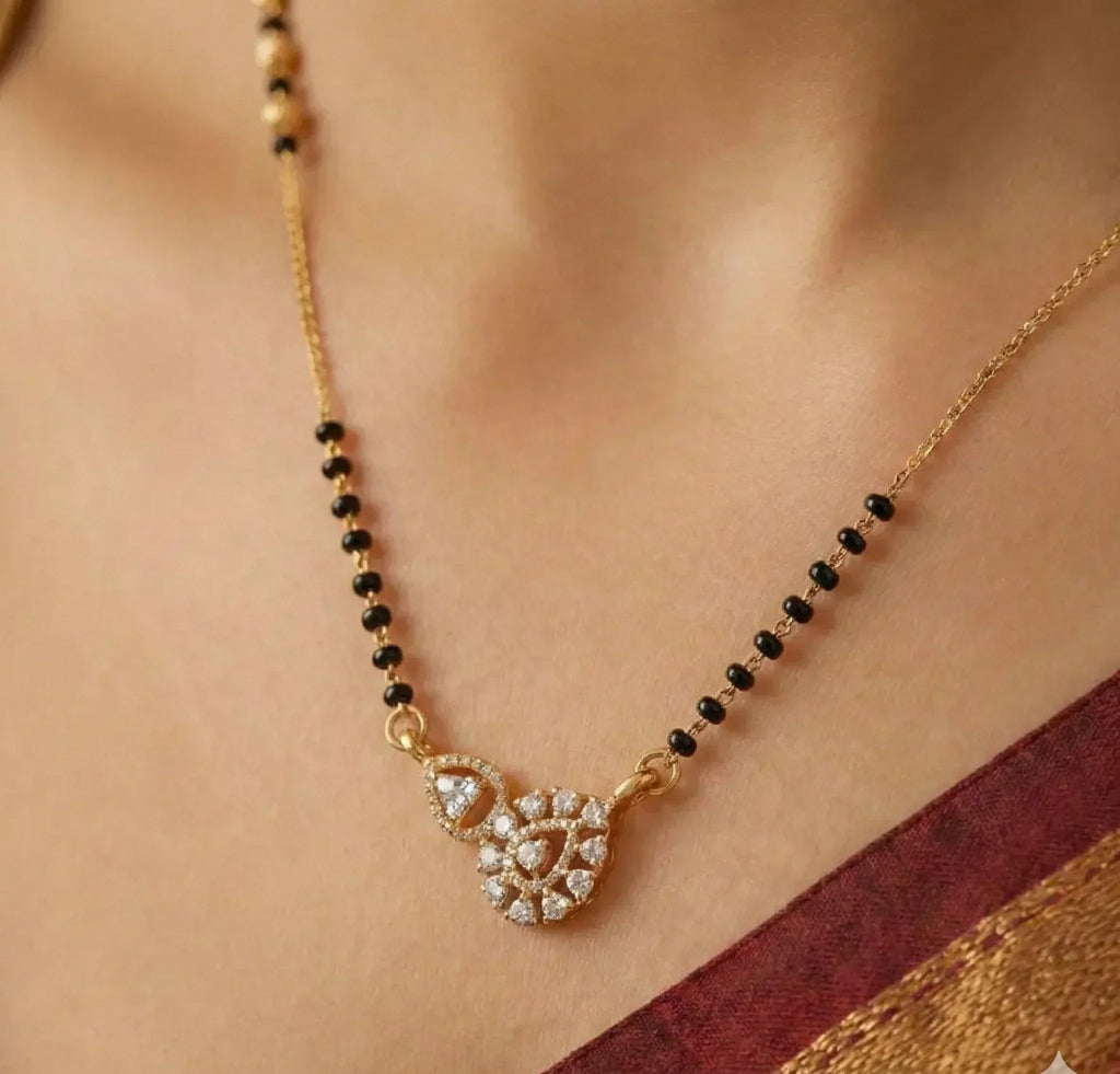 Gold necklace with black beads and a heart-shaped pendant on a person wearing a saree.