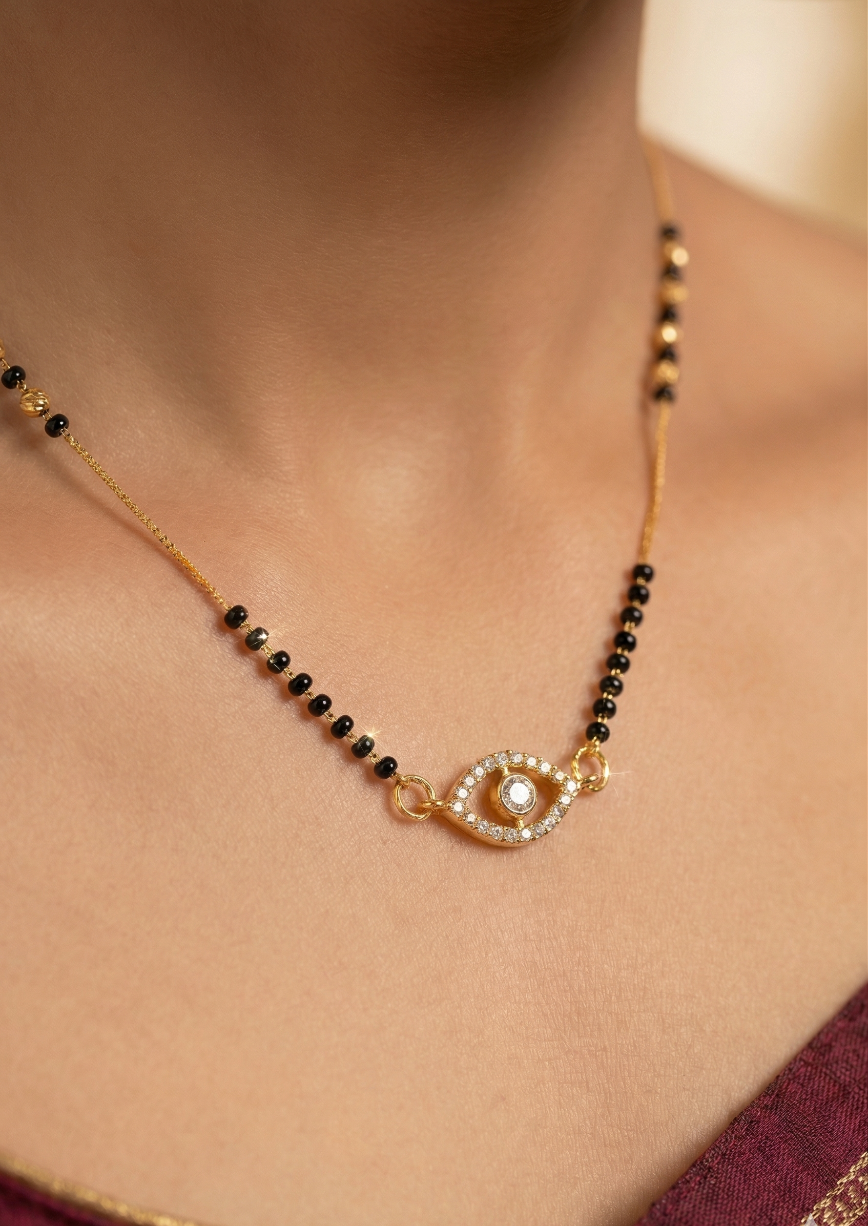 Gold necklace with black beads and an eye-shaped pendant on a person wearing a red garment.