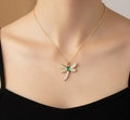 Gold necklace with a dragonfly pendant featuring green and clear stones on a mannequin.