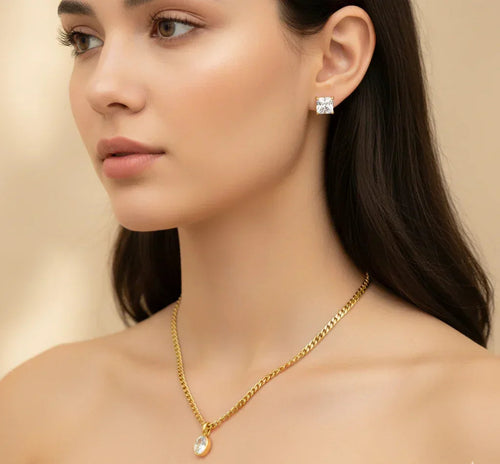 Woman wearing a gold necklace and diamond earrings on a beige background