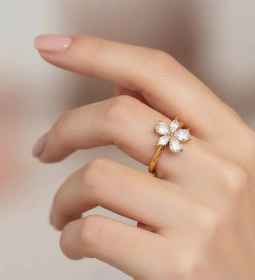 Hand wearing a gold ring with a diamond flower design on a blurred background